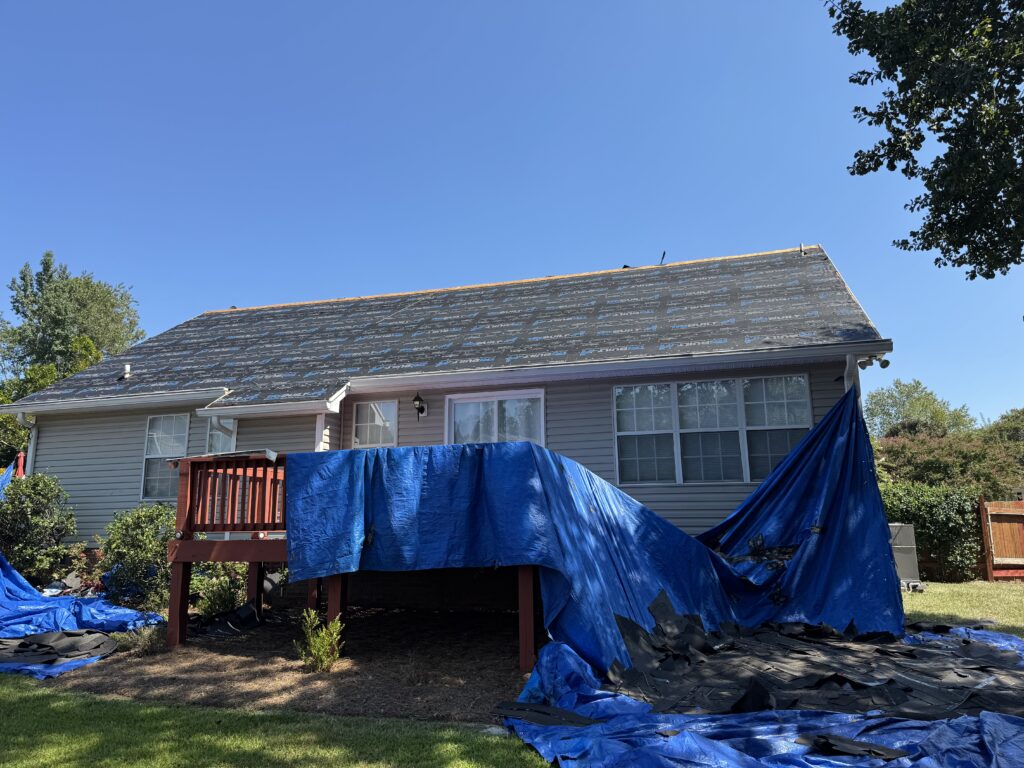 Roof replacement in progress with underlayment installed and landscaping protected to prevent debris and water damage during installation.
