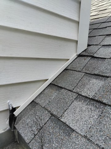 Repaired: new sidewall flashing run tight up the wall-to-roof line and tucked in behind the siding, so runoff is carried down onto the shingles and out instead of behind the wall