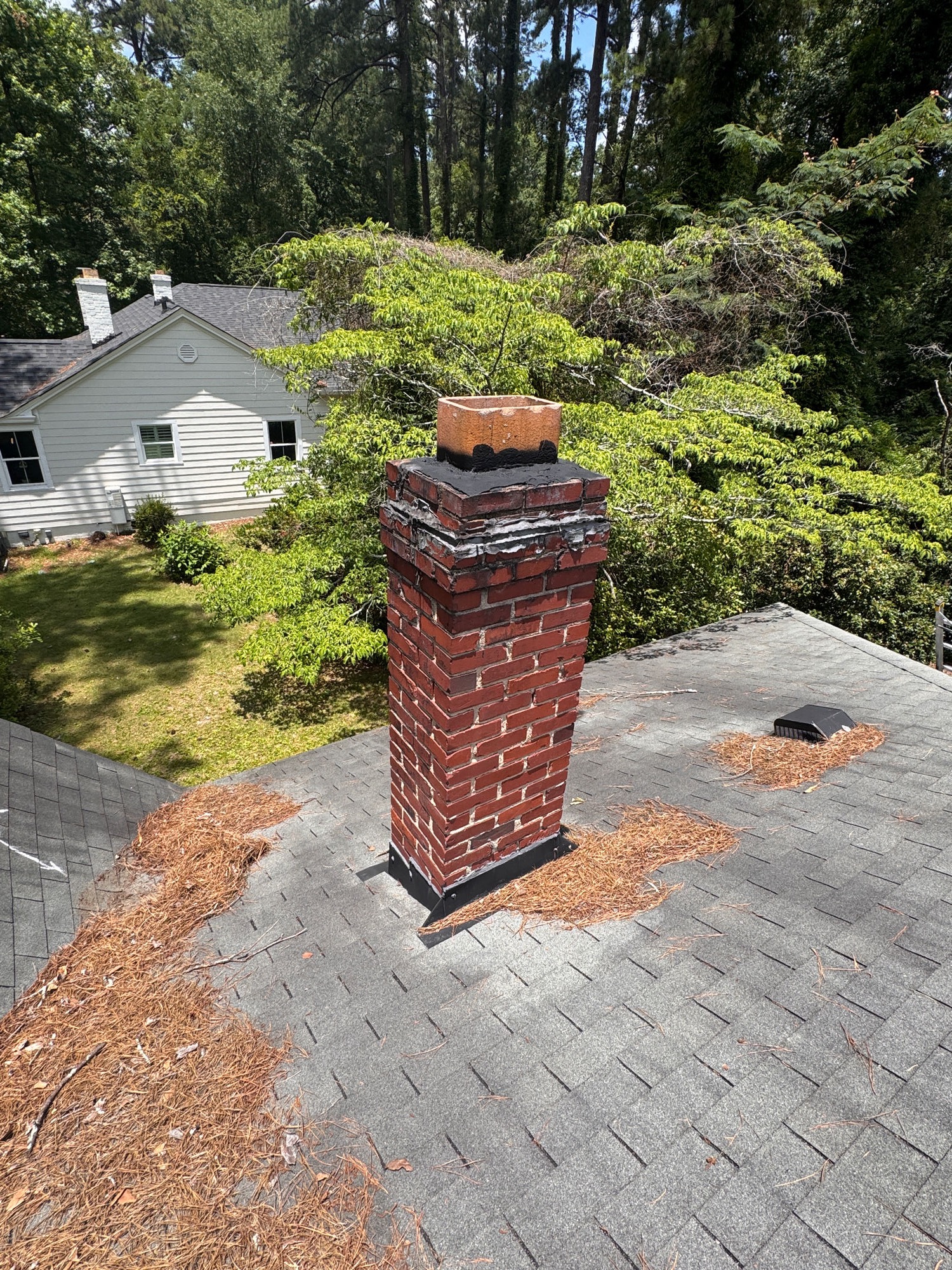 The chimney taken care of top to bottom: the cracked crown sealed over and the base flashing re-set flat against the shingles all the way around