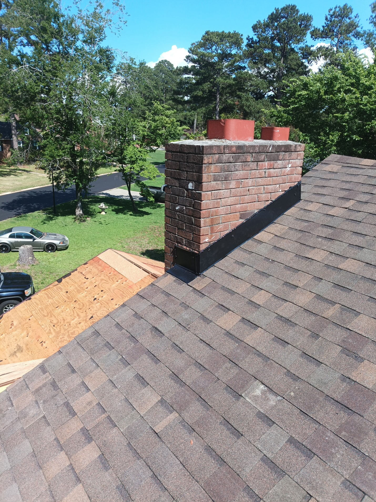 New architectural shingles tied in around the chimney with fresh flashing, while decking continues on the adjoining slope