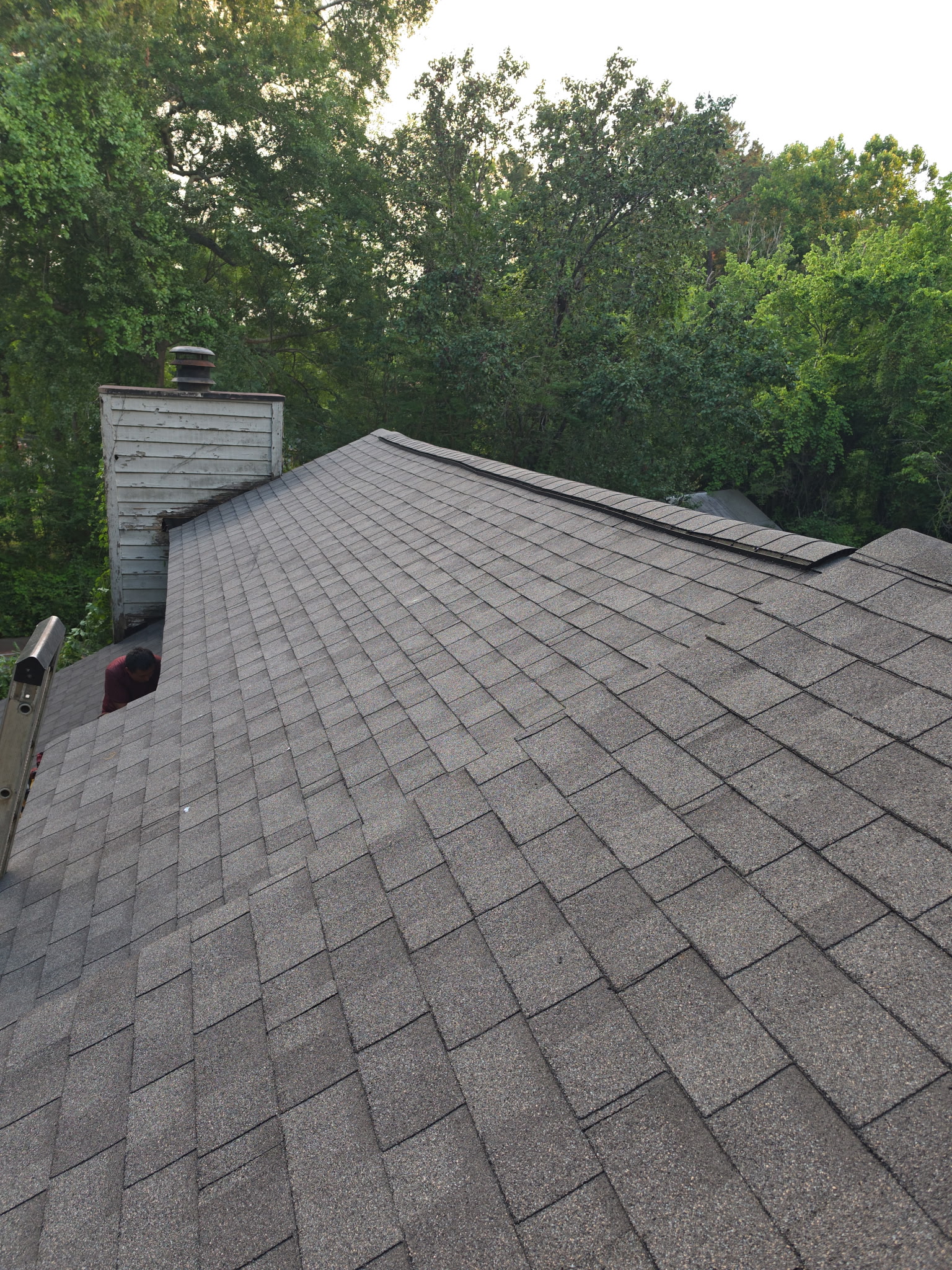 Finished: crisp new shingle slopes tied in cleanly around the chimney and the adjoining rooflines