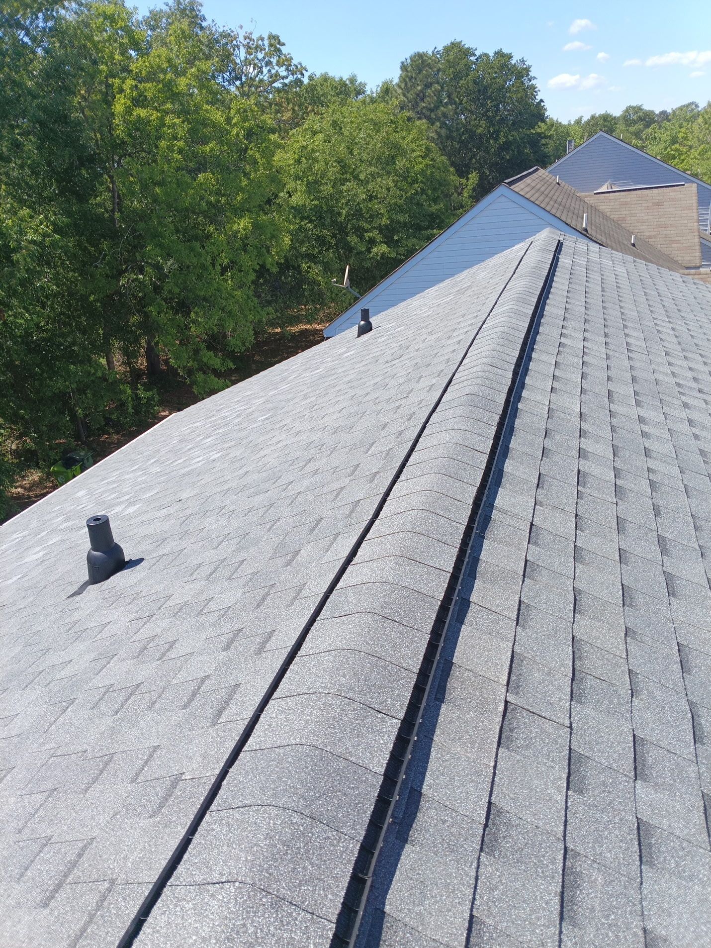 Finished: the rear slopes in new architectural shingles, new boots set on the plumbing vents, and