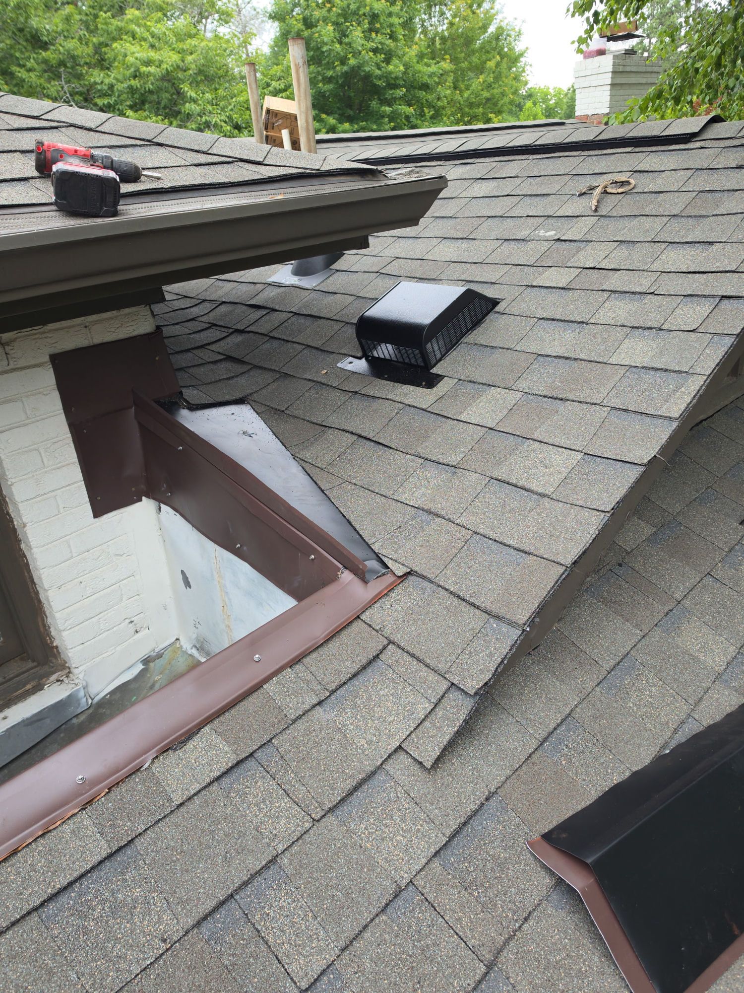 Installation underway: new shingles laid in around a new roof vent, with the chimney flashing set