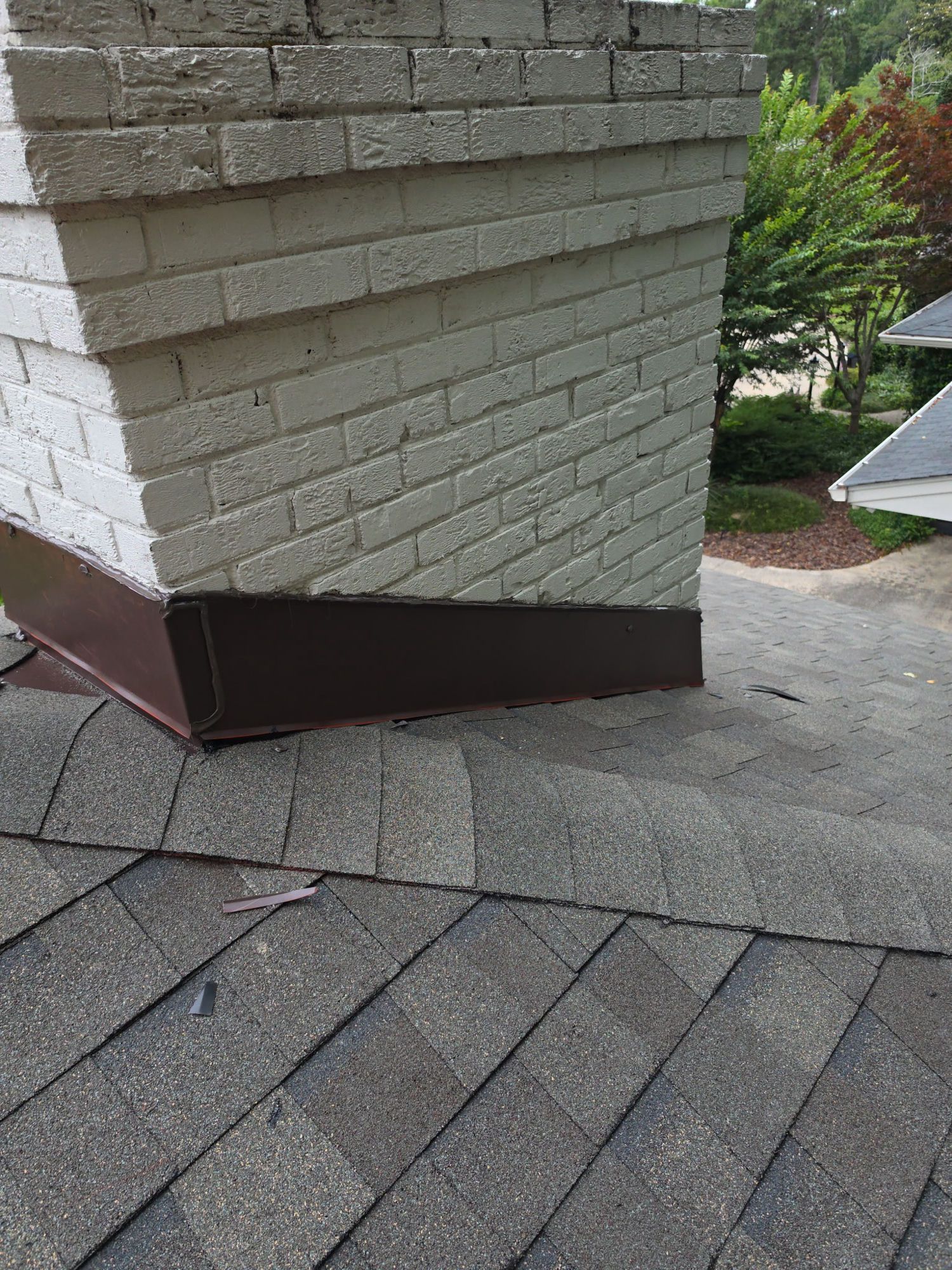 Finished: new counter-flashing wrapped tight around the base of the painted brick chimney, with the