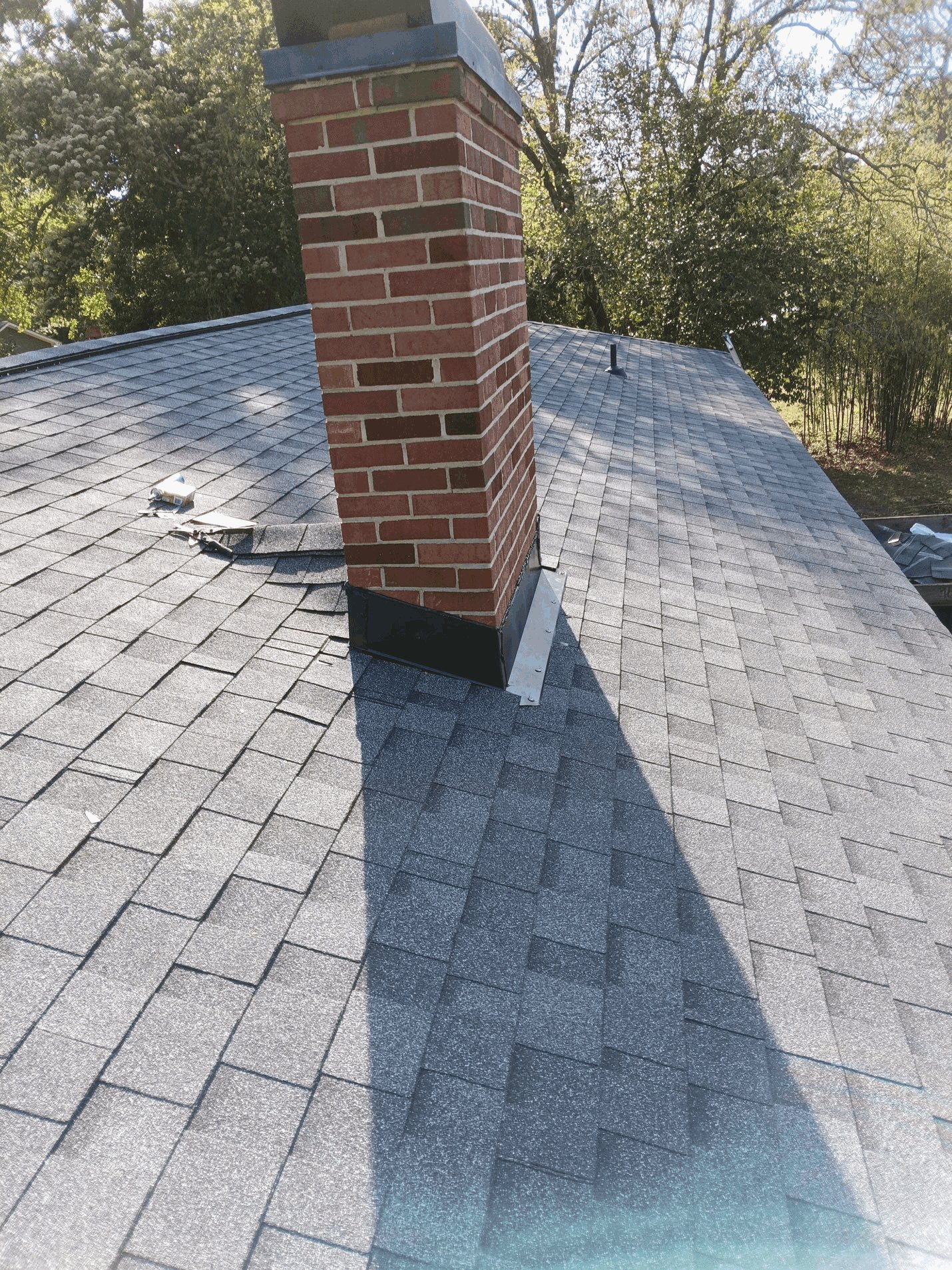 The new chimney flashing with the shingles worked in around it, as the crew finishes the slope above