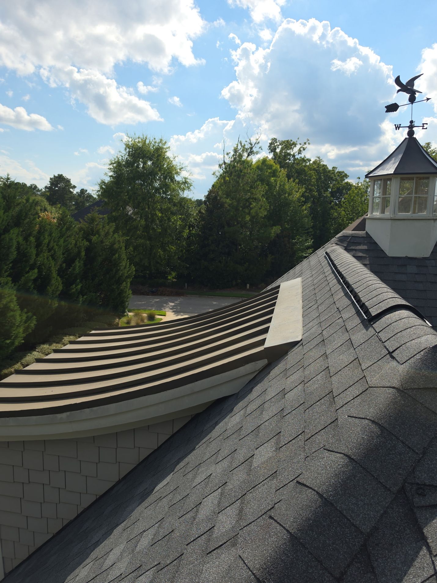 Finished: the new shingles tied in against the curved metal bay roof, with a vented ridge leading