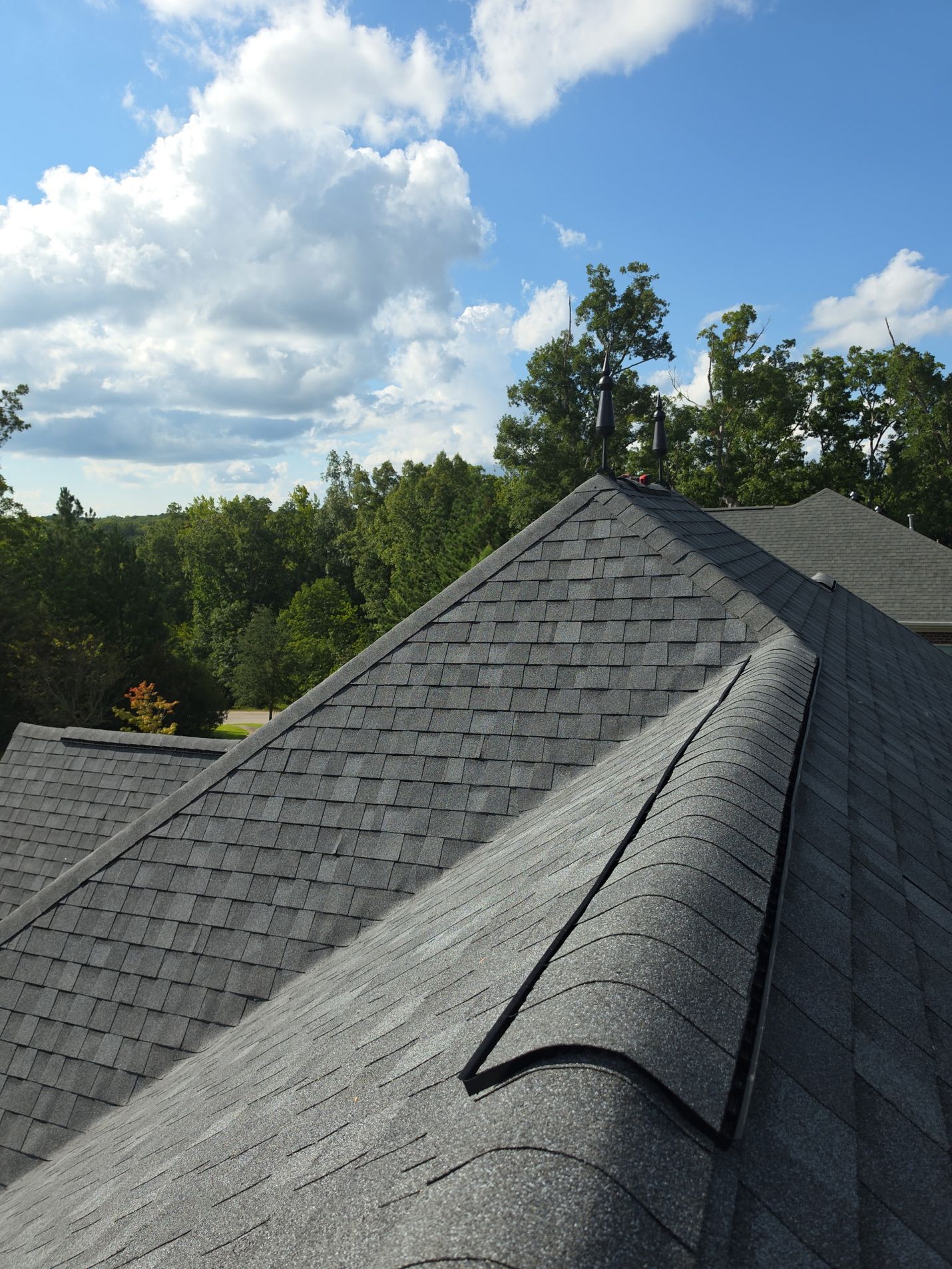 Finished: the vented ridge cap running up the main hip toward the finials, with the new shingle