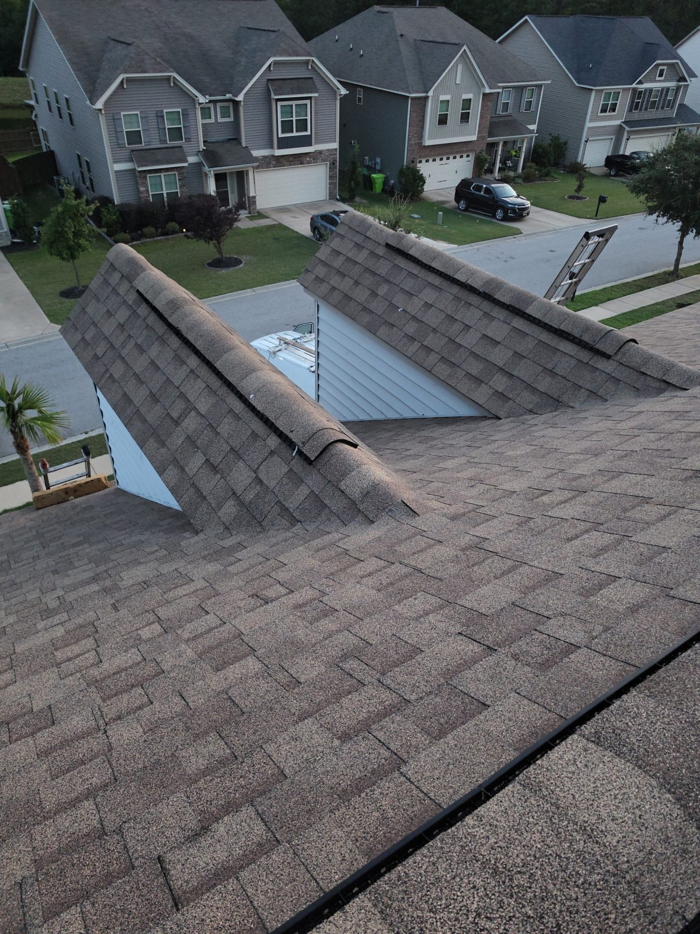 Finished: both front dormers in new architectural shingles, each with its own vented ridge cap,