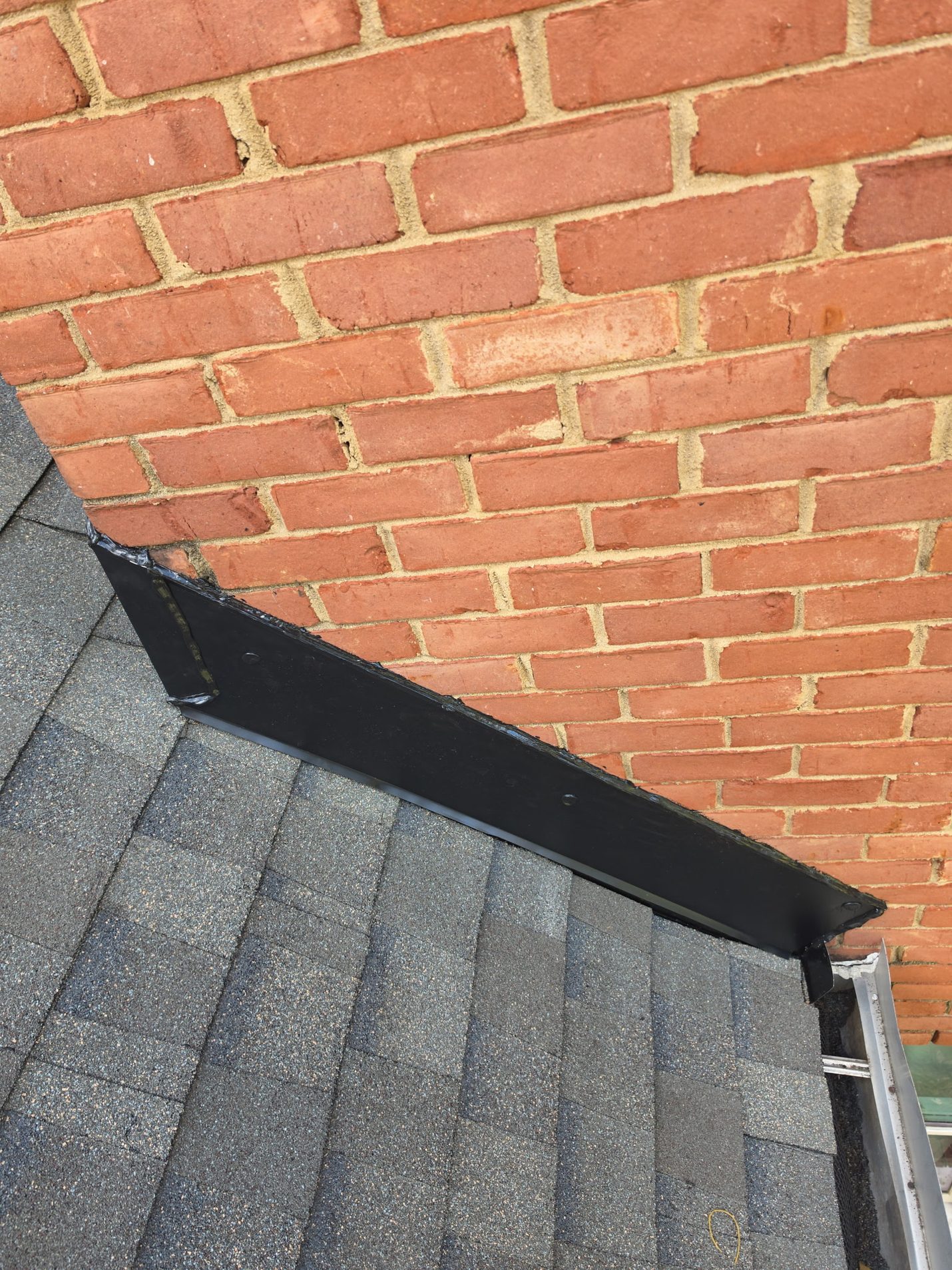 Finished: new black metal flashing fastened and sealed along the base of the brick chimney, with