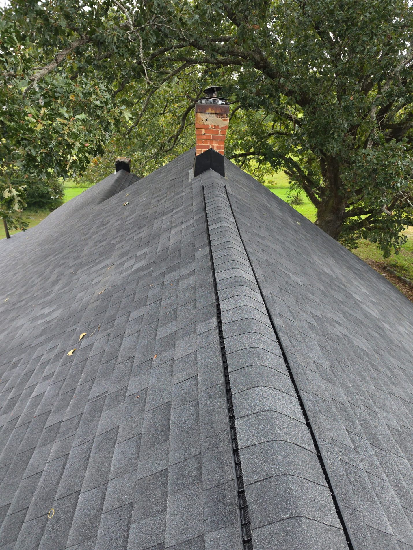 Finished: the ridge capped in new shingles over a continuous ridge vent, running back to the